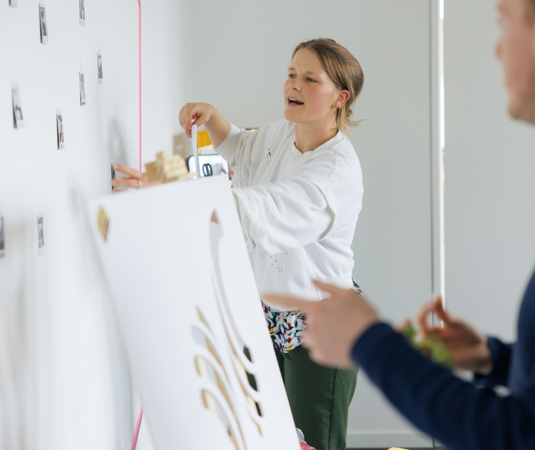 PD-Mitarbeitende kleben in einem Workshop Bilder an eine Wand.