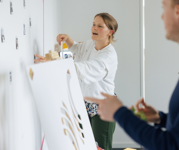 PD-Mitarbeitende kleben in einem Workshop Bilder an eine Wand.