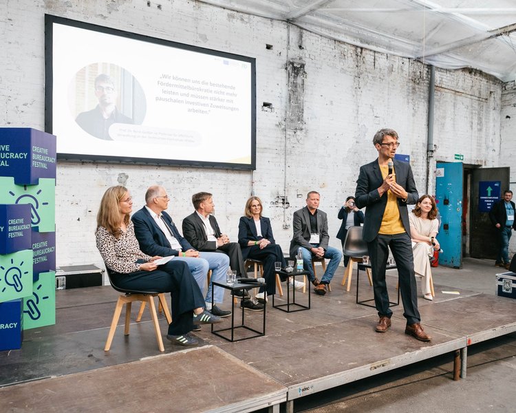 Eine Gruppe sitzt auf der Festival-Bühne, während ein Mann mit Mikrofon spricht. Im Hintergrund läuft eine Präsentation, auf der Bühne ist CBF-Dekoration sichtbar.