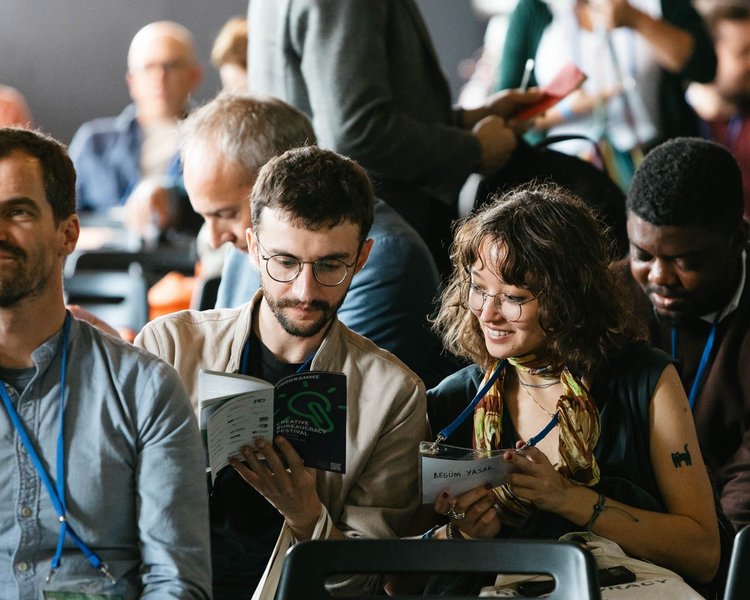 Das Bild ist auf das Publikum gerichtet. Im Fokus sind ein Mann und eine Frau die mit Freude in das CBF-Programmflyer schauen.