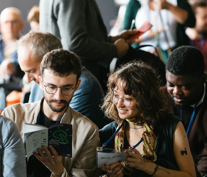 Das Bild ist auf das Publikum gerichtet. Im Fokus sind ein Mann und eine Frau die mit Freude in das CBF-Programmflyer schauen.