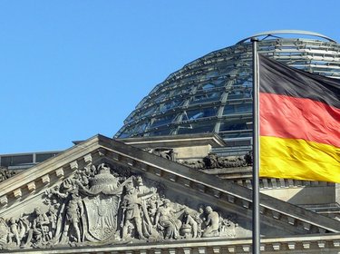 Die Bundestagskuppel mit einer Deutschlandflagge im Vordergrund.