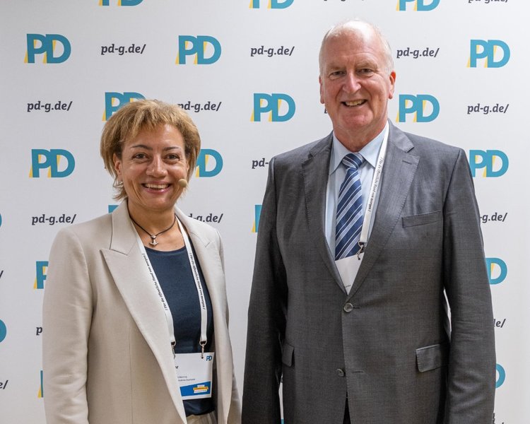 Yvonne Balzer (PD-Standortleitung) und Rainer Mues (Abteilungsleitung, Ministerium der Justiz des Landes Nordrhein-Westfalen) vor einer PD-Logo-Wand