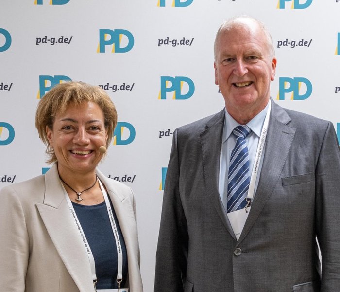Yvonne Balzer (PD-Standortleitung) und Rainer Mues (Abteilungsleitung, Ministerium der Justiz des Landes Nordrhein-Westfalen) vor einer PD-Logo-Wand