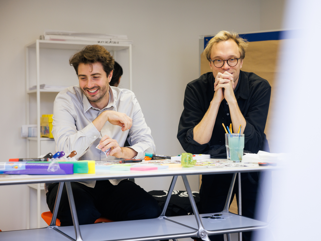Zwei Mitarbeitende stehen an einem Tisch, nutzen Post-its und Stifte für kreative Arbeit und lachen dabei