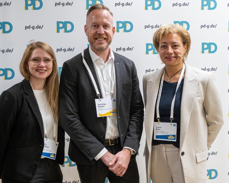Myriel Schiffbauer (Managerin, PD – Berater der öffentlichen Hand GmbH), Lars Philipp Tolckmitt (Behördenleitung, Landesamt für Finanzen NRW) und Yvonne Balzer (PD-Standortleitung) vor einer PD-Logo-Wand