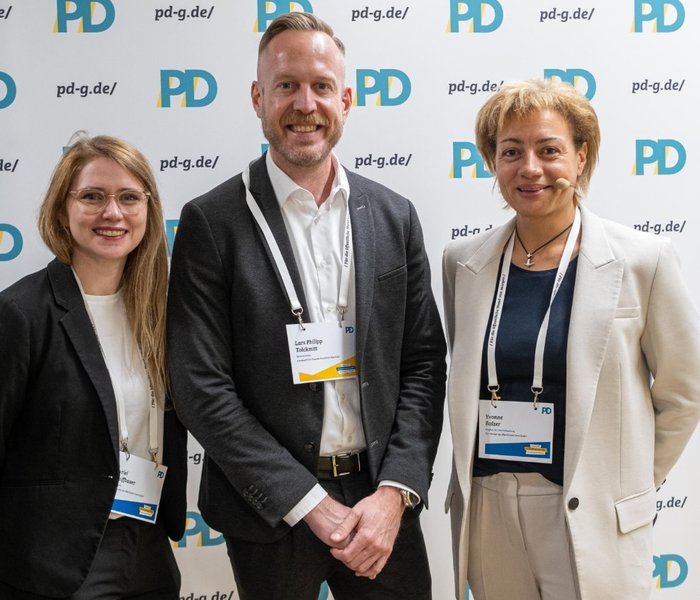 Myriel Schiffbauer (Managerin, PD – Berater der öffentlichen Hand GmbH), Lars Philipp Tolckmitt (Behördenleitung, Landesamt für Finanzen NRW) und Yvonne Balzer (PD-Standortleitung) vor einer PD-Logo-Wand
