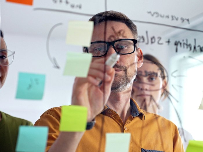 Ein Mann schreibt mit einem schwarzen Stift auf eine Glaswand voller Post-Its