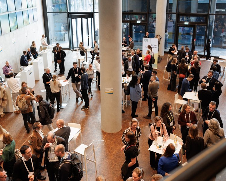 PD-Mitarbeitende stehen zusammen an Stehtischen und unterhalten sich im Foyer einer Firmenevent location