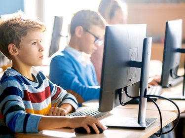 Schulkinder sitzen im Unterricht vor Computerbildschirmen.