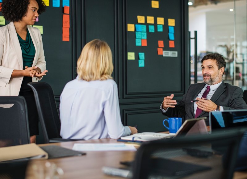 Drei Personen in einer Besprechung vor Kanban-Wand.