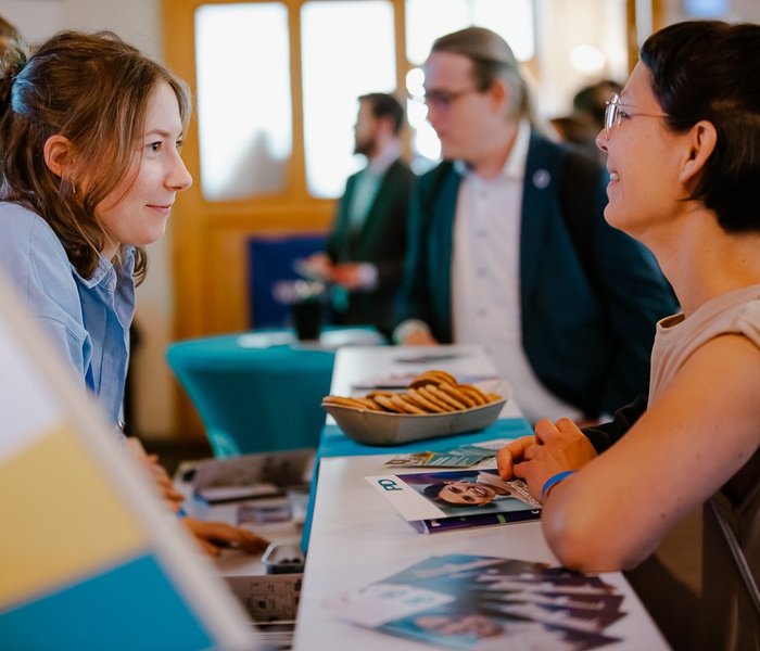 Eine PD-Mitarbeiterin und eine interessierte Person unterhalten sich. Sie stehen sich am PD-Stand gegenüber.
